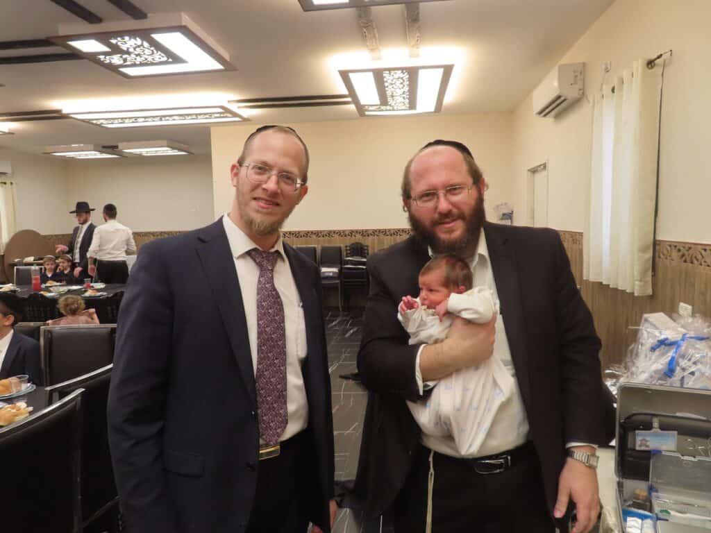 המוהל הרב דב קליין מחזיק תינוק לצד האב
